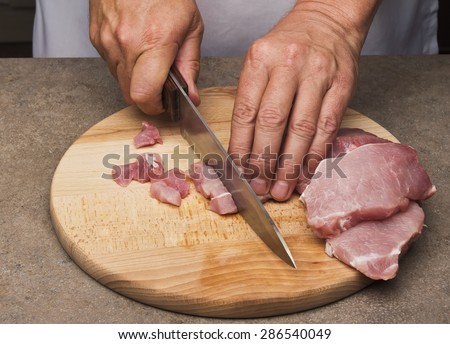 Hands of a man preparing meat  in a kitchen slicing lean meat on a wooden board