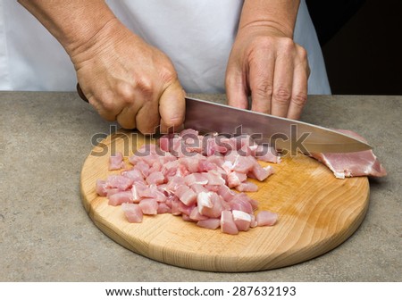 Hands of a man preparing meat in a kitchen slicing lean meat on a wooden board
