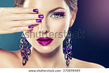 beautiful   girl model with fashion make-up and purple manicure on nails . Jewelry and cosmetics , large violet earrings