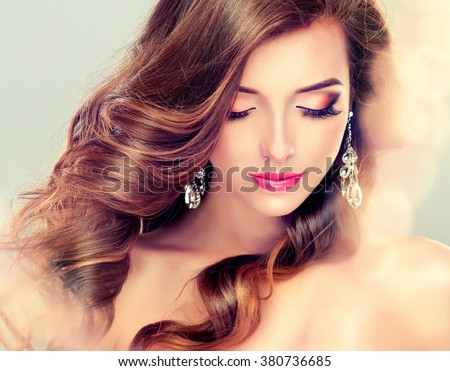 Beautiful model brunette with long curled hair and jewelry earrings