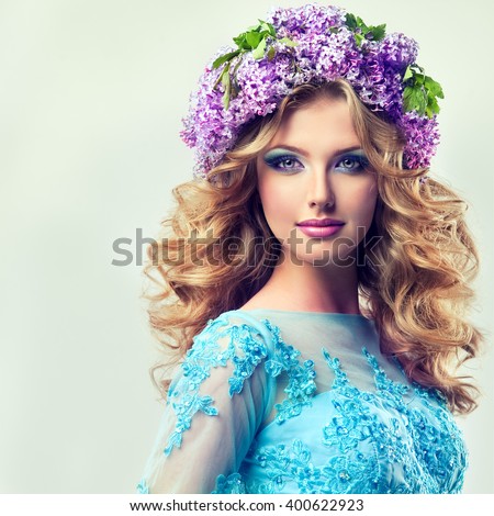 Beautiful model blonde girl   of flowers lilac  on the head    ,with curly long hair.  Girl spring . Summer image .Makeup,cosmetics,beauty. wreath of lilac on the head .