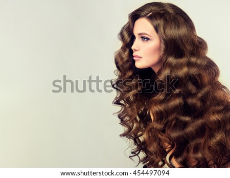 Brunette  girl with long  and   shiny wavy hair .  Beautiful  model with curly hairstyle