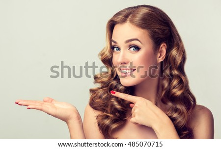 Woman surprise showing product .Beautiful girl with curly hair pointing to the side . Presenting your product. Expressive facial expressions