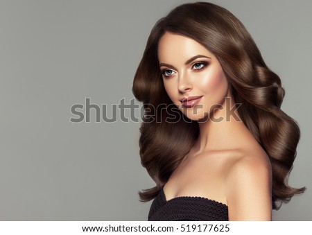 Brunette girl with long and shiny wavy hair. Beautiful model with curly hairstyle.