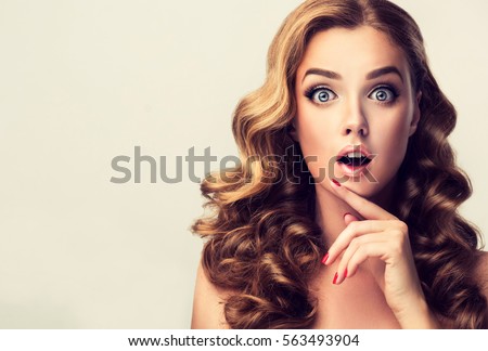 Woman surprise showing product .Beautiful  surprised ,  wonder  and shocked  girl  with curly hair  . Presenting your product. Expressive facial expressions