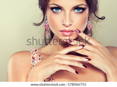 Beautiful model girl with pink metallic manicure on nails . Fashion makeup and cosmetics . Pink dress with rhinestones and pink earrings jewelry .