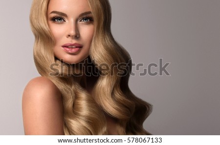 Blonde  girl with long  and  volume shiny wavy hair .  Beautiful  woman model with curly hairstyle .