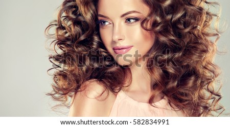 Brunette  girl with long  and  volume shiny wavy hair .  Beautiful  model with curly hairstyle .