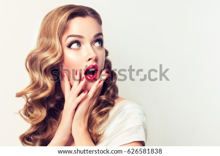 Shocked and surprised girl screaming and  looking to the side presenting  your product . Curly hair woman amazed .Beautiful girl  with curly hair and red nails manicure. Expressive facial expressions