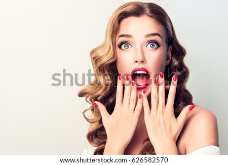 Shocked and surprised girl screaming covering  mouth her hands . Curly hair woman amazed .Beautiful girl  with curly hair and red nails manicure. Presenting your product..Expressive facial expressions