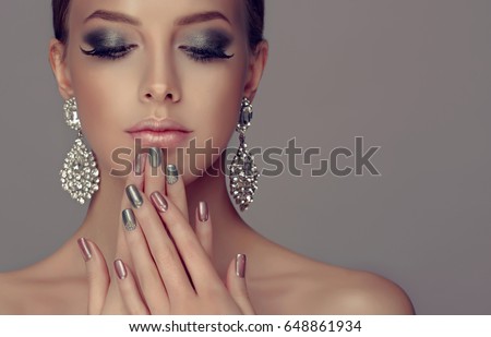 Beautiful model girl with pink and silver  metallic manicure on nails . Fashion makeup smokey eyes and cosmetics . Big silver diamond Shine  earrings jewelry .