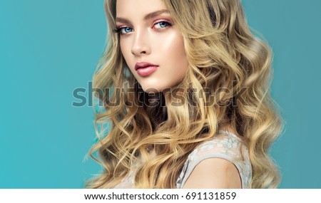 Blonde fashion  girl with long  and   shiny curly hair .  Beautiful  model  in light blue dress with wavy hairstyle .