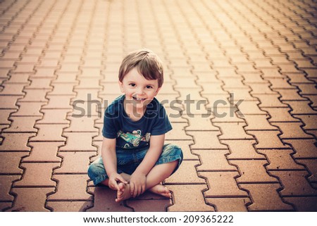 smiling little boy sitting on the ground and looking into the camera