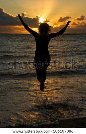 Silhouette of young woman on sunset in the sea, view of young jumping lady at beach on gold sunset, woman jumping in the sunset on the beach, girl running in the water, sunset hour, dramatic sunset