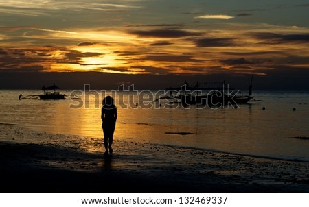 One alone woman going on coastline in colorful dramatic sunset golden hours with golden sky and boats background, one woman on sunset, golden sunset hours in tropics, amazing sunset
