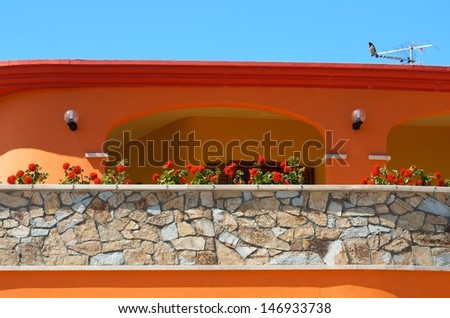 Colorful typical sardinian house with the red flowers and blue sky background, orange house fragment close up in sunny day, colorful sardinian house, nice building in Porto Torres, Sardinia, Italy,