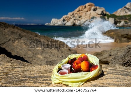 Fresh fruits peaches,cherries with the juice in plastic bag on a stone with Capo Testa rock view in Sardinia,backpacker lunch fruits and juice with view to the sea, mixed fruits in a plastic bag