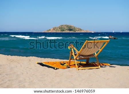 Beach chair on yellow sand beach with blue sky,Beach Chair on day on the beach with blue sky background and blur boats, small island far away,summer holiday in Sardinia, one chair in front of blue sky