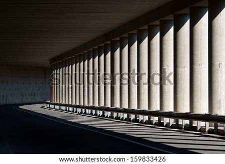 Road with the bridge arch and columns details. Architectural element with the selective focus. Columns in shadows on sunny daylight. Road and architecture fragment. Architecture background