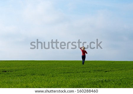 One woman in green grass field with blue sky background, saturated. Single woman in the field selective focus. Green field and one woman. Romantic atmosphere wit sunny day background. Calm day