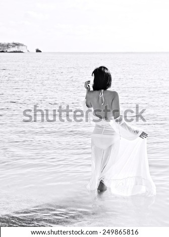 Young beautiful woman in white dress going to the sea, high key, alone woman near the sea in black and white photo, artistic photo of young woman, woman figure in nature, holidays, romantic holidays