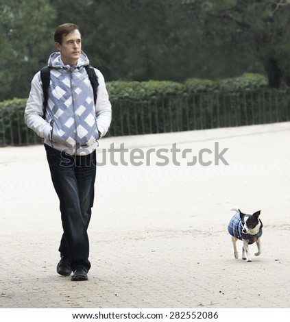 Man and dog walking in the park. Man and dog in same jacket walking in the park dark cloudy day.