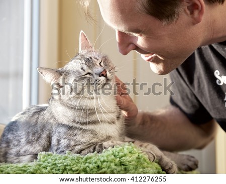 Cat and man, portrait of happy cat with close eyes and young man , man playing with the cat. Handsome Young Animal-Lover Man, Hugging and Cuddling his Gray Domestic Cat Pet