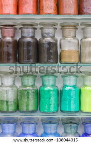 Colorful glass bottles of paint pigments on glass shelves