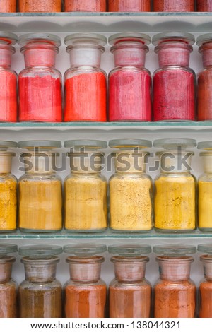Colorful glass bottles of paint pigments on glass shelves