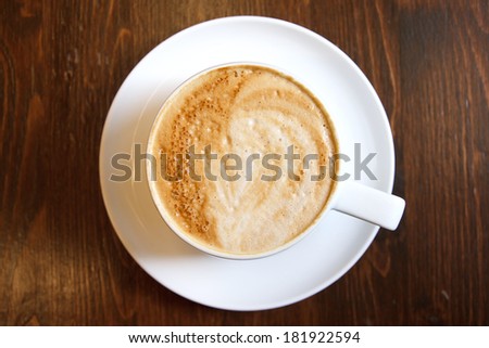 Classic foamy cappuccino in on a dark grained wood table. Detail. From above.