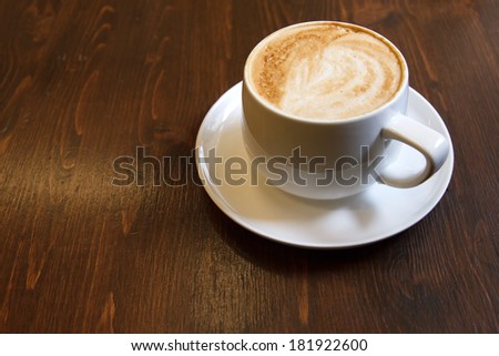 Classic foamy cappuccino in on a dark grained wood table. Detail. Space for text.