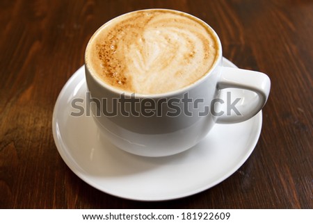 Classic foamy cappuccino in on a dark grained wood table. Detail. From above. Detail.