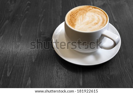 Classic foamy cappuccino in color on a black and white grained wood surface. Space for text.