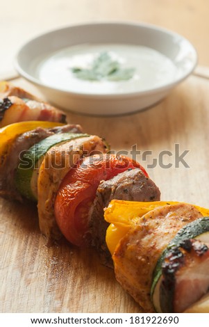 Detail of mixed grilled meats on a skewer. Sitting on a wood board with white sauce behind.