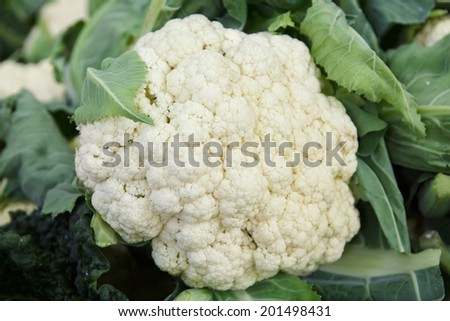 Whole fresh cauliflower with mixed out of focus vegetables in the background.