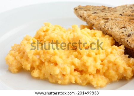 Soft scrambled eggs  next to sliced brown toast on a white plate.