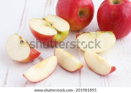 Pink lady apples cut on a painted white rustic wood table.