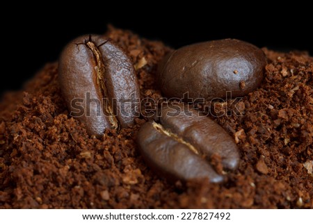 Three roasted coffee beans on ground coffee. Black background.