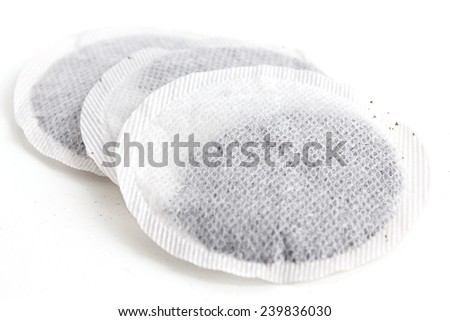 Round black tea bags on white surface.