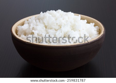 Rustic bowl of cooked white rice on dark surface.