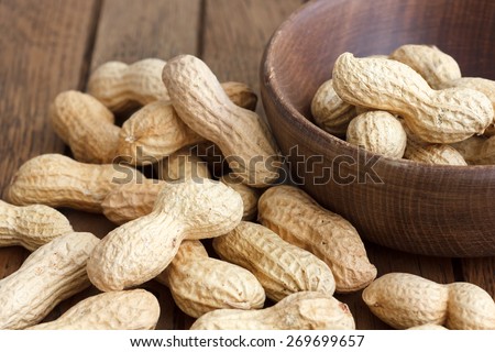 Rustic wood bowl of peanuts in shells. In perspective.