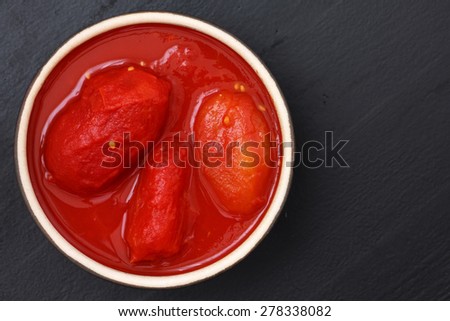 Whole canned tomatoes in dish from above on black wood.
