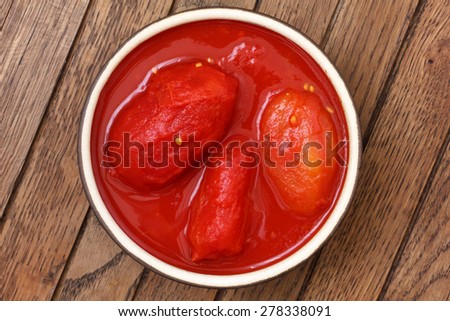 Whole canned tomatoes in pottery dish from above on wood.