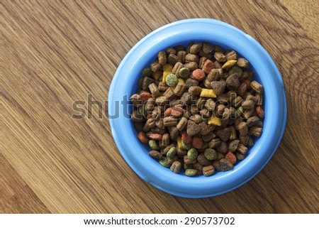 Dry cat food in blue bowl isolated on wood floor from above.
