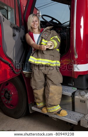 A female firefighter standing in the door of a fire truck.