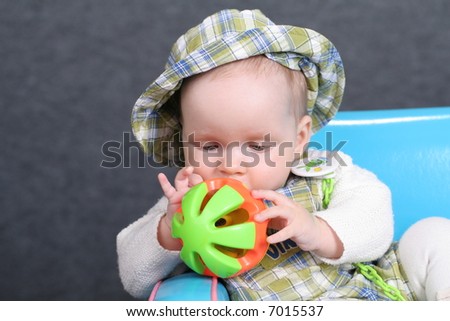 Cute small kid with hat tries to eat plastic vegetable (toy)