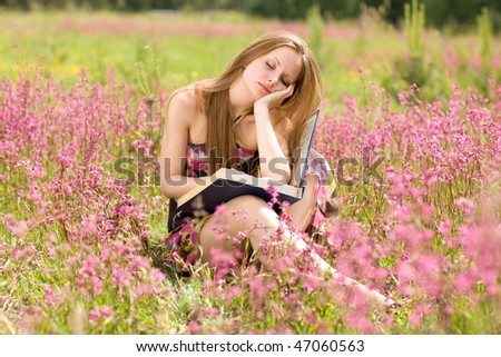 Cheerful girl reads a book in meadow with pink flowers