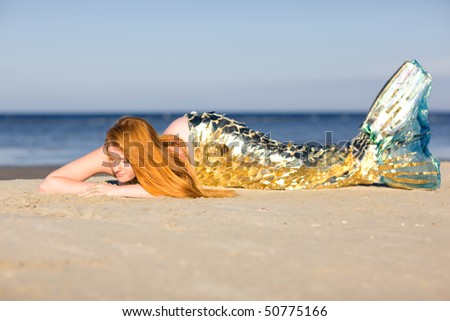 Orange haired mermaid with tail on the beach