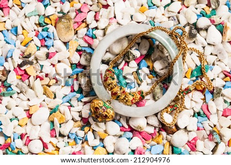 Gold necklace with heart pendants and jade bracelet on stone background.