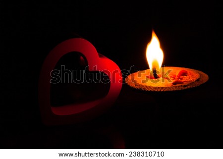 A burning candle and red heart in dark.